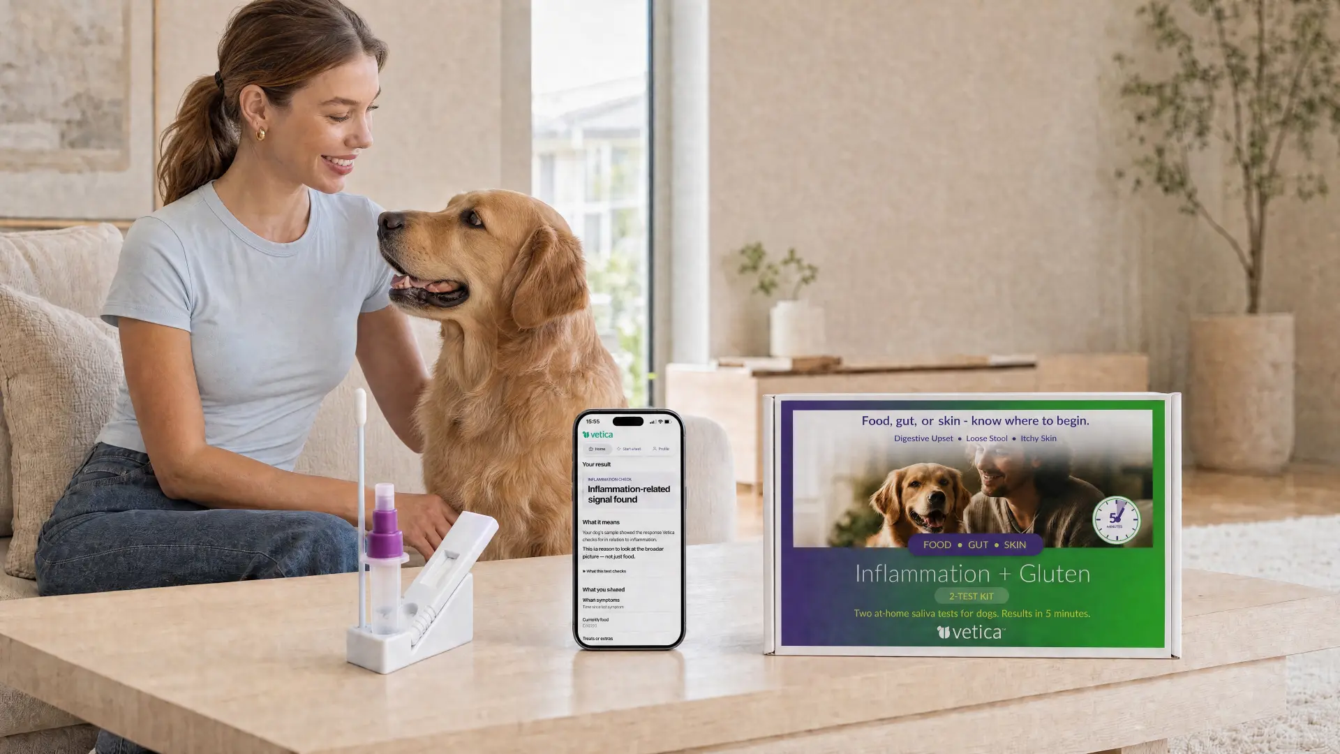 A woman smiling at her golden retriever on the sofa, with a Vetica test, a phone showing a result and the 2-Test Kit box on the table